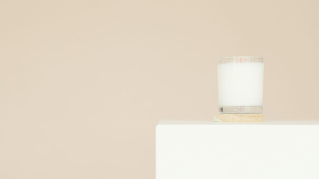 A minimalist white candle on a square platform with beige background.